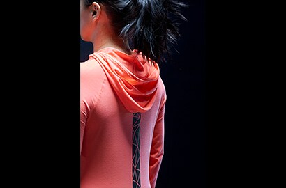 Woman standing in dark wearing pink hoodie with 3M Scotchlite Black Stretch Reflective stripe down center back.