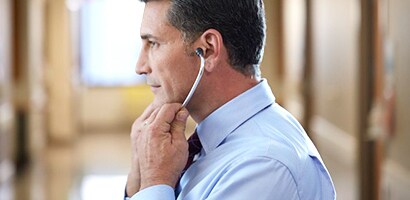 Médico a colocar corretamente um estetoscópio Littmann, com as olivas viradas para a frente.
