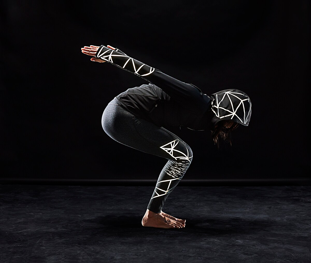 Athletic woman in yoga pose wearing activewear with 3M Scotchlite C790 Carbon Black Stretch Reflective Material illuminated.