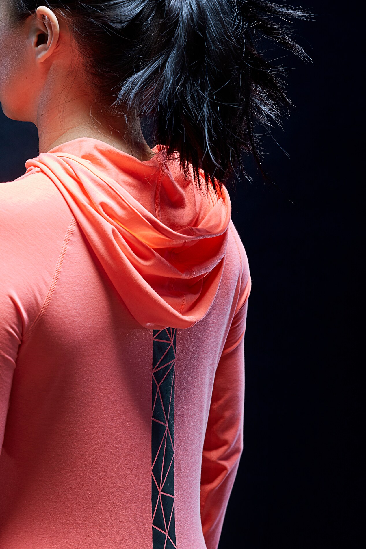 Woman standing in dark wearing pink hoodie with 3M Scotchlite Black Stretch Reflective stripe down center back.
