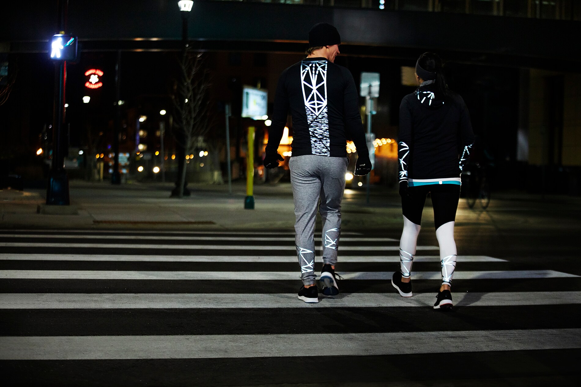 Homem e mulher a correr, paisagem urbana noturna, equipamento iluminado pelo o 3M™ Scotchlite™ C790 Refletor Elástico Carbon Black.
