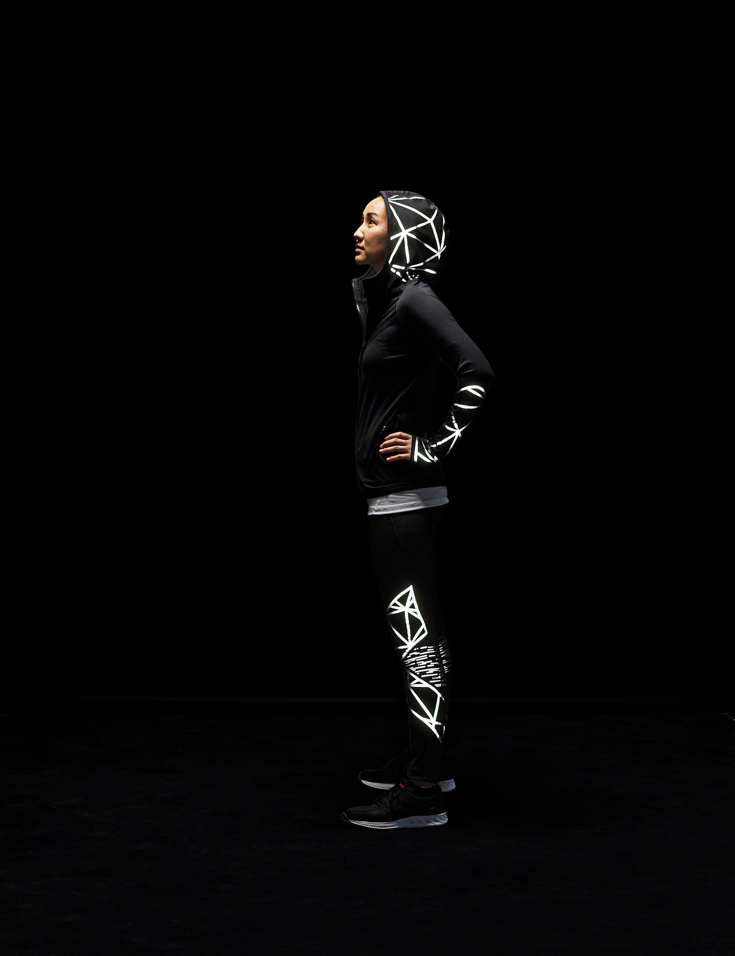 Woman standing in dark wearing jacket, pants illuminated by 3M Scotchlite Black Stretch Reflective.
