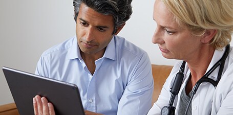 Médico ausculta e mostra a aplicação no tablet ao doente
