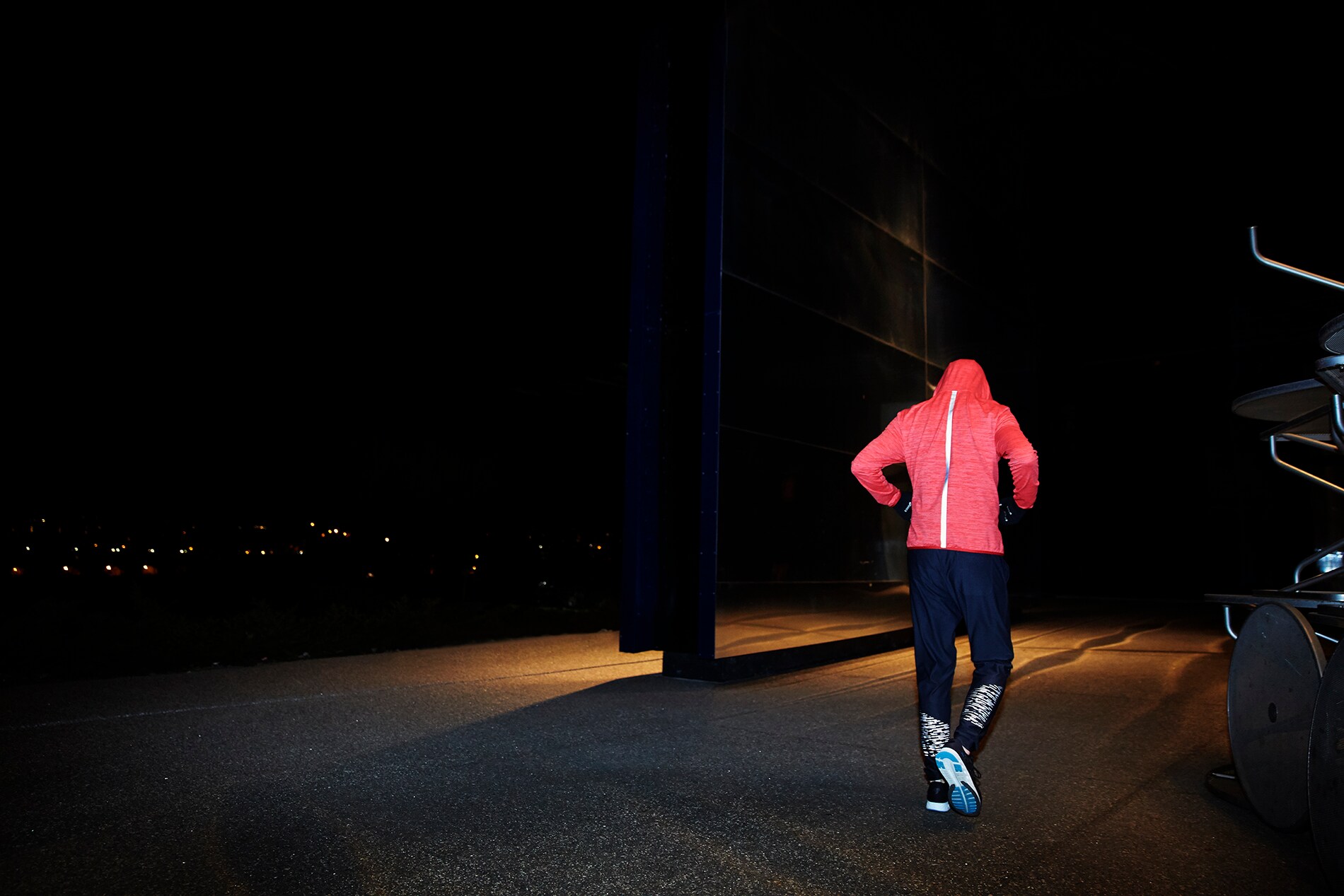 Illuminated Black Stretch Reflective on back of man walking next to wall of mirrors at night.
