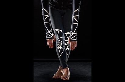 Athletic woman leaning forward wearing activewear with 3M Scotchlite C790 Carbon Black Stretch Reflective Material lit up.