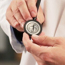 Grande plano de um médico a segurar o auscultador de um Estetoscópio 3M Littmann com o selo Littmann no diafragma.