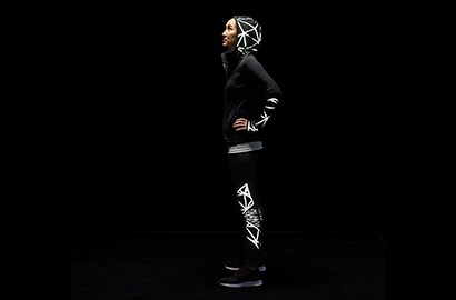Woman standing in dark wearing jacket, pants illuminated by 3M Scotchlite Black Stretch Reflective.