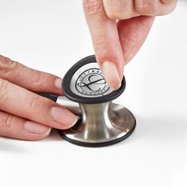 Dedos a removerem o diafragma sintonizável da campânula de um Estetoscópio 3M Littmann Classic III.