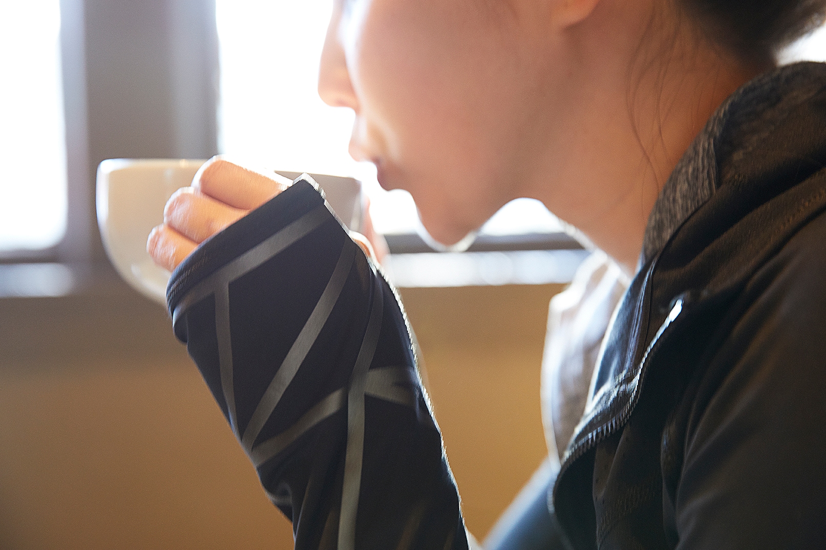 Woman drinking coffee, close up of Scotchlite Black Stretch Reflective on sleeve of activewear jacket.