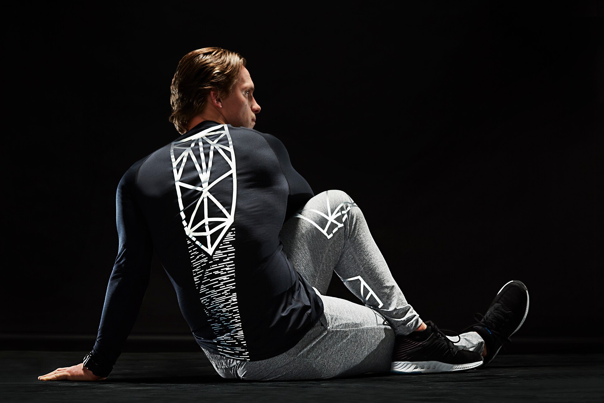 Athletic male stretching on floor wearing activewear 3M Scotchlite C790 Carbon Black Stretch Reflective Material illuminated.
